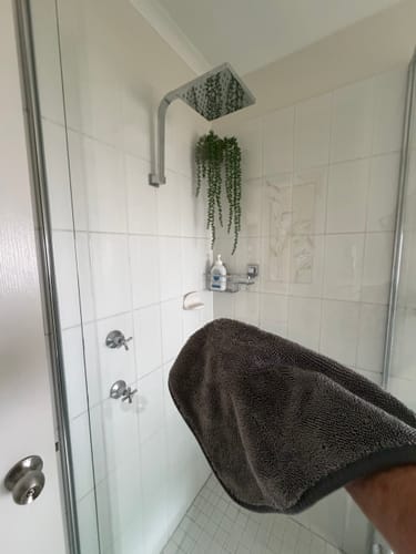Customer holding a dark KoalaCloth in a clean, tiled shower, showing the shiny fixtures.