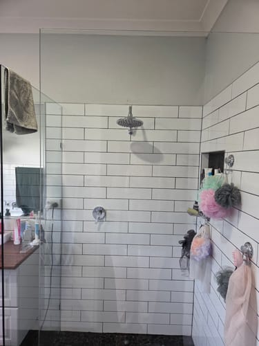 Customer's shower with a sparkling clean glass panel and white tiles after using a KoalaCloth.