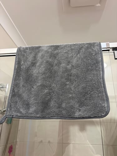 Customer's grey KoalaCloth hanging over a glass shower door in a bathroom.